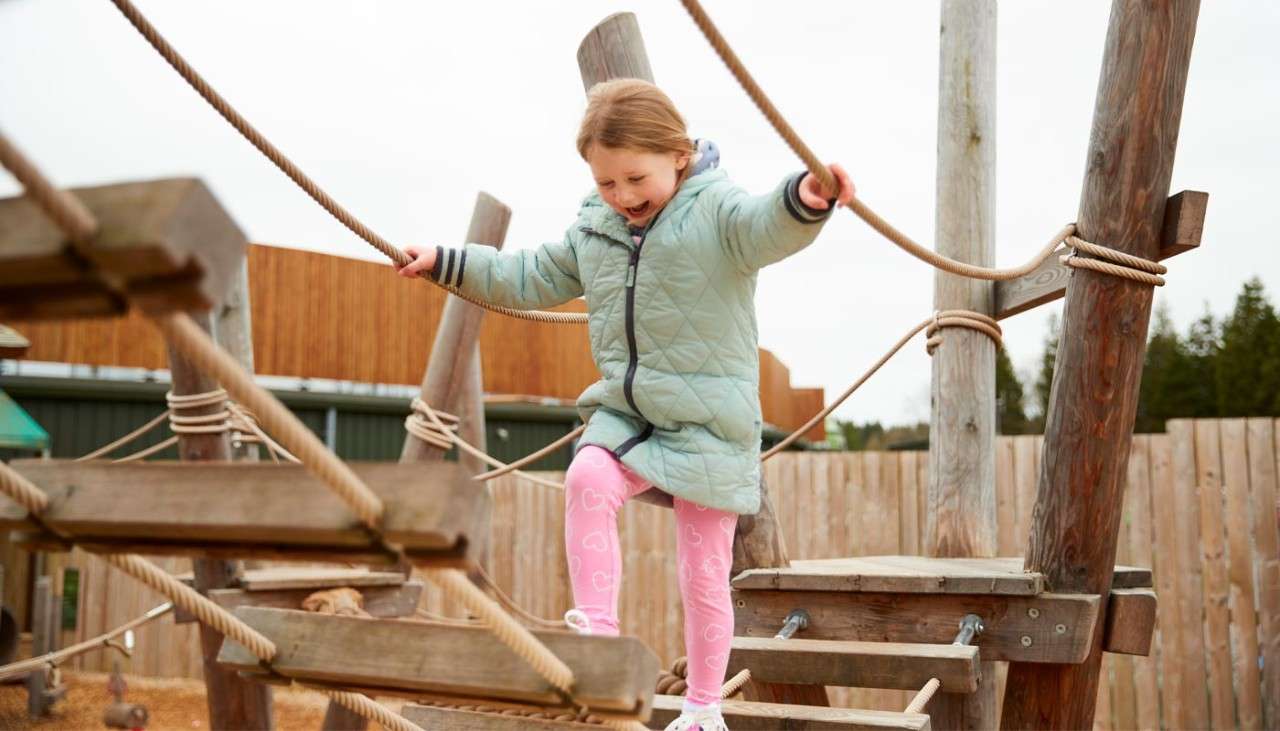 Young girl walking over a wooden bridge on a play ground