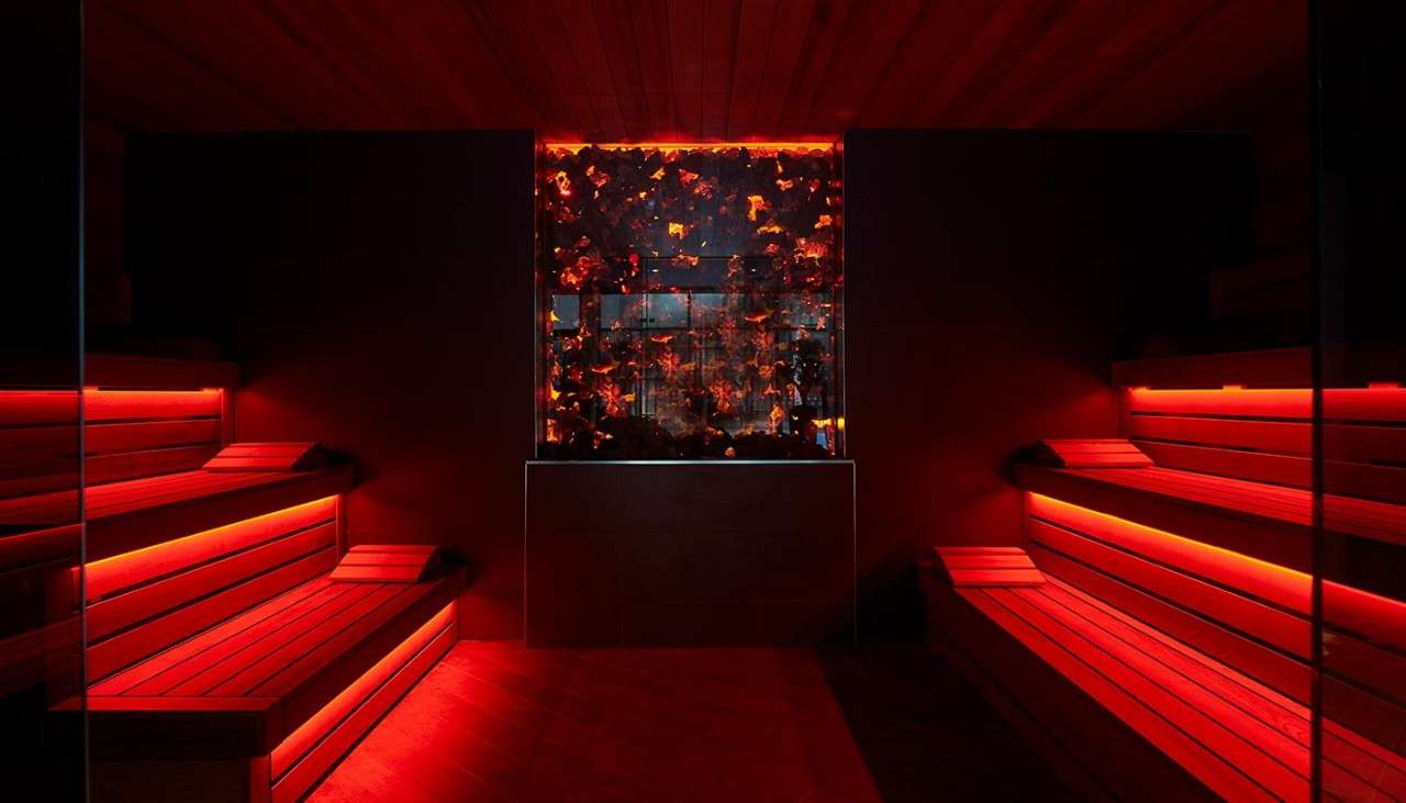 Lava Sauna illuminated in red with a coal themed glowing window display and stacked wooden benches.