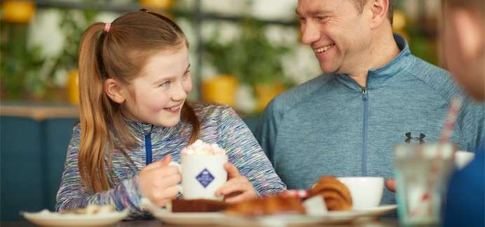 A man and girl sitting enjoying cake, coffee and hot chocolate