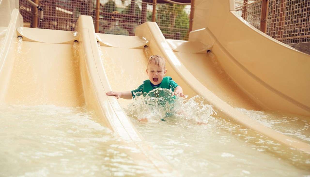 A toddler wearing a life jacket sliding down a small waterslide.