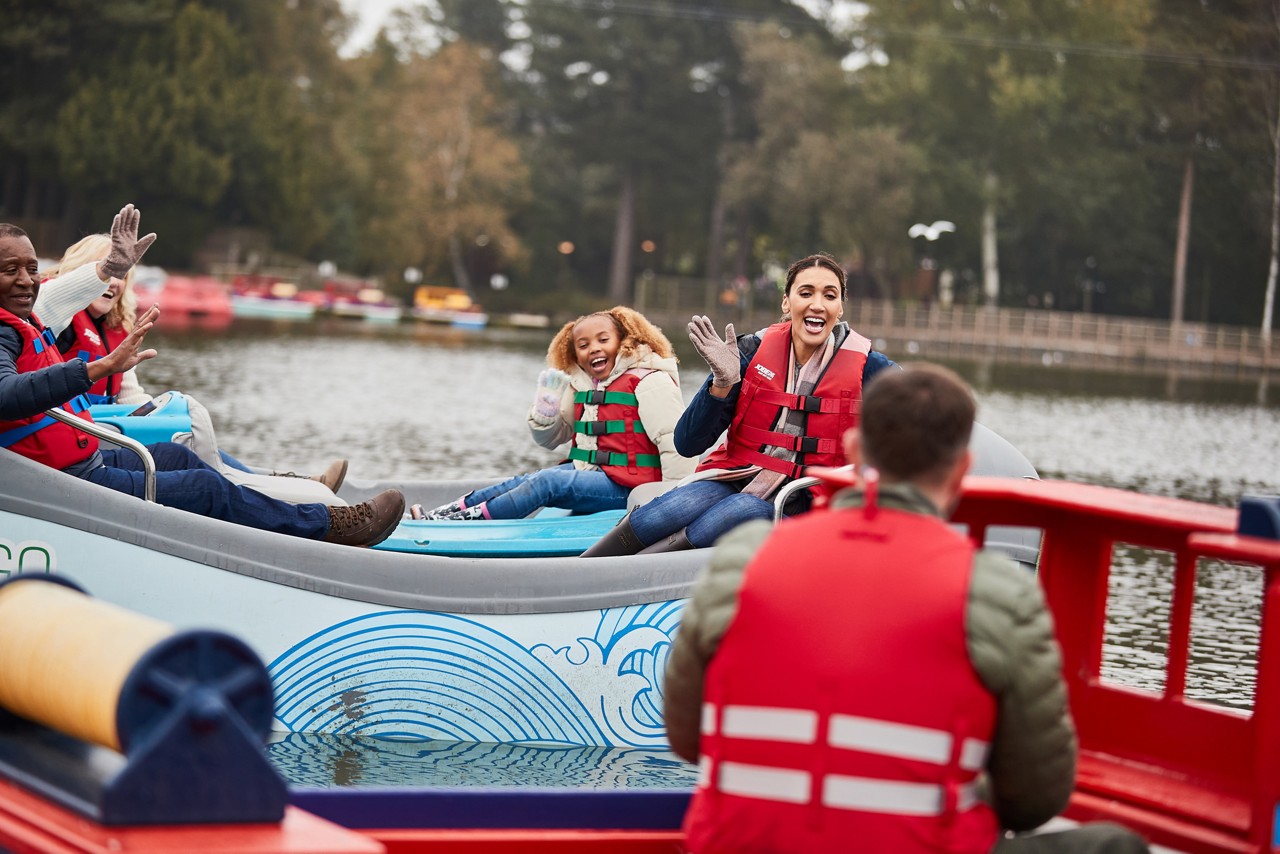 A family waving at each other on the lake whilst they are in boats.