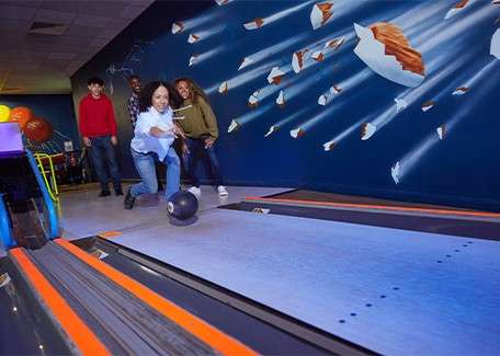 A teenage girl bowling with her family.