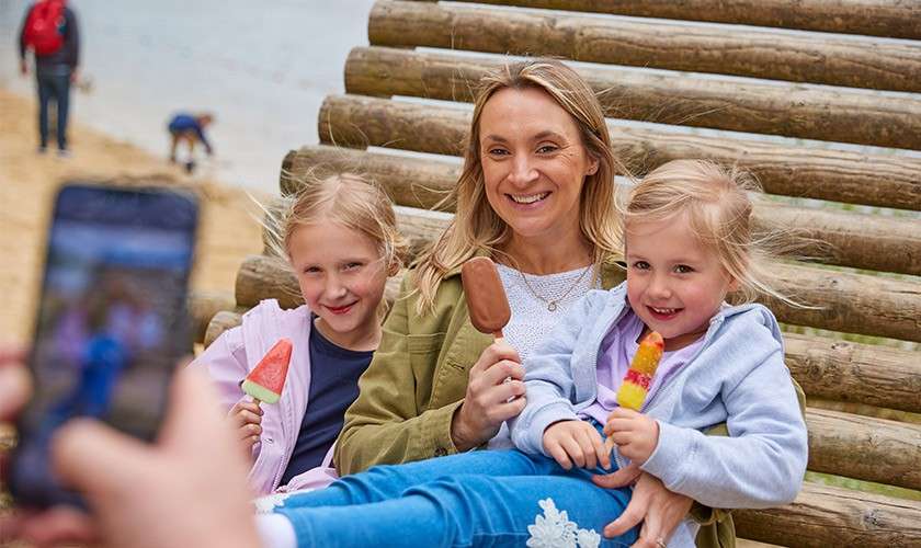 A mum and her daughters sat on the beach having their photo taken whilst holding ice creams.