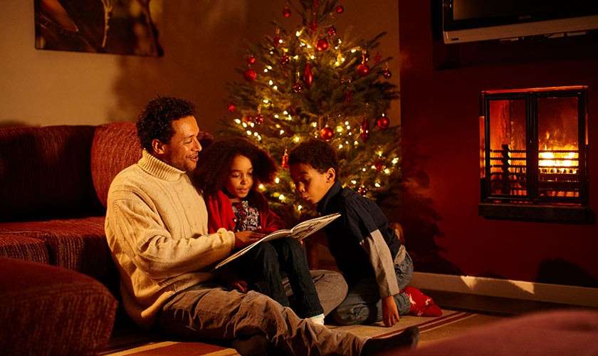 Family in lodge in front of log fire and Christmas tree