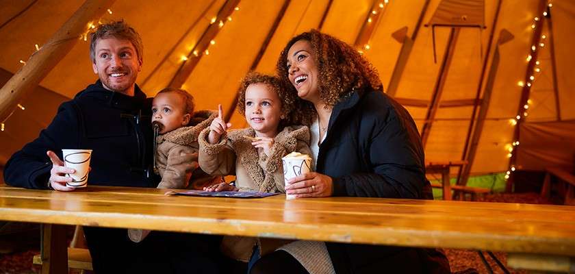 A family enjoying hot drinks in the seating area of the Forest Fayre Tipi.
