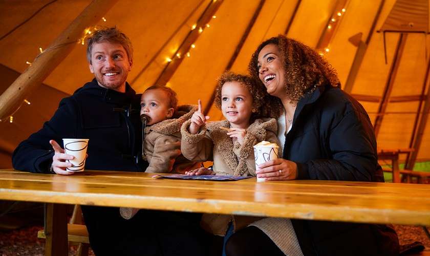 A family of four smiling and enjoying hot drinks at the Festive Fayre.