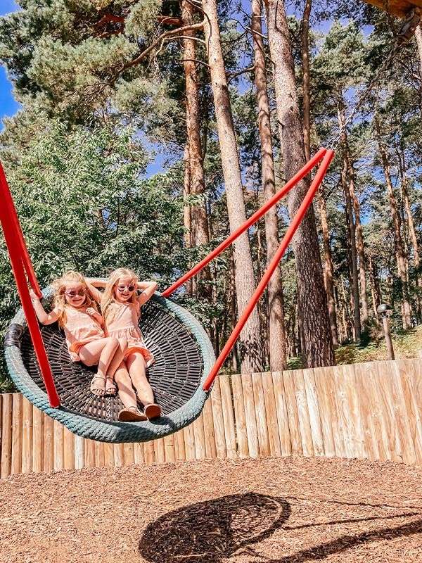 Two girls on a swing in the outdoor playground.