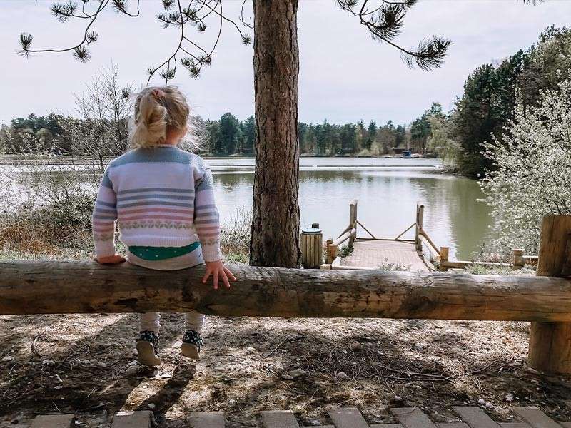 A little girl sat on a log by the lake.