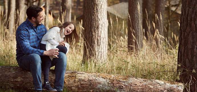 A father and daughte laughing on a bench outside.