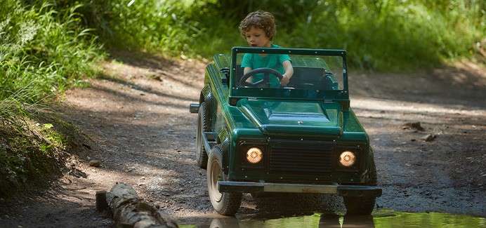 A child driving a small off road car through the forest.