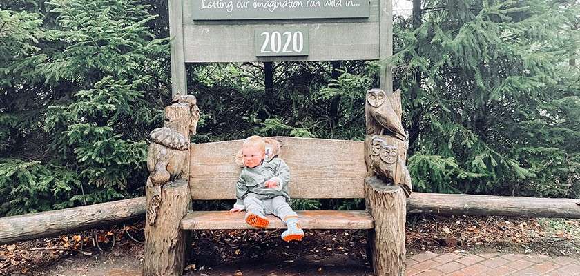 A toddler sat on a bench underneath a sign that says "2020".