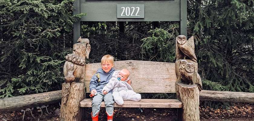 A toddler and a baby sat on a bench underneath a sign that says "2022".