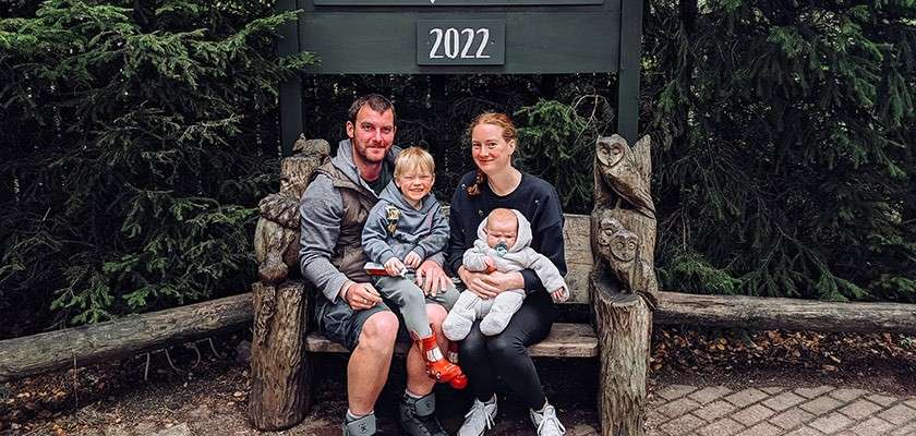 Parents holding their toddler and baby sat on a bench underneath a sign that says "2022".