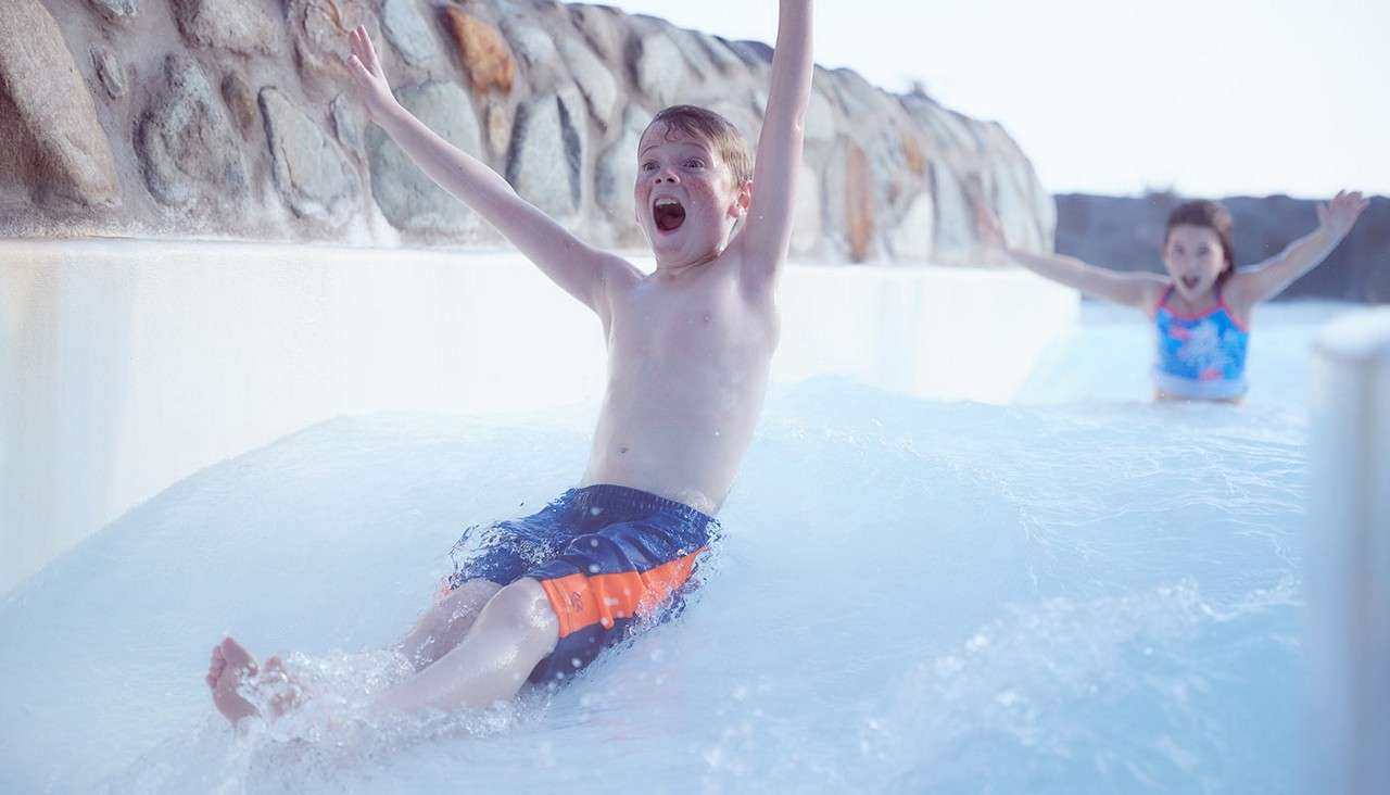 A boy sliding down the rapids waving his arms in the air. 