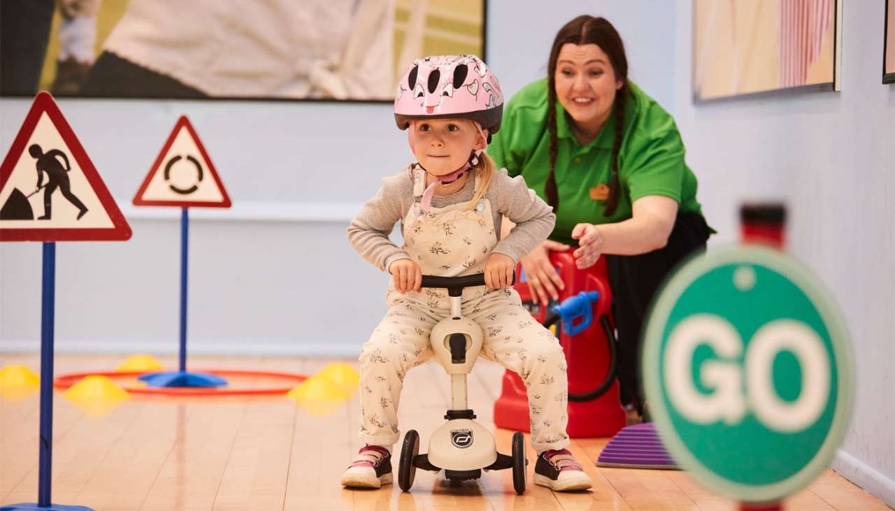 Little girl riding a little scooter around an indoor track