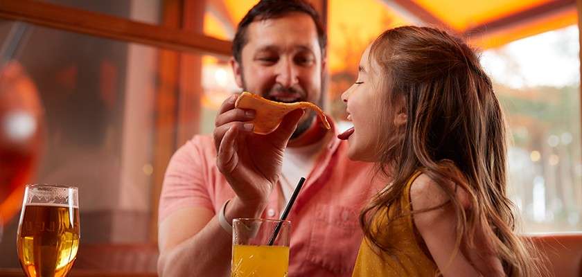 A father feeding his daughter a slice of pizza at a restaurant.