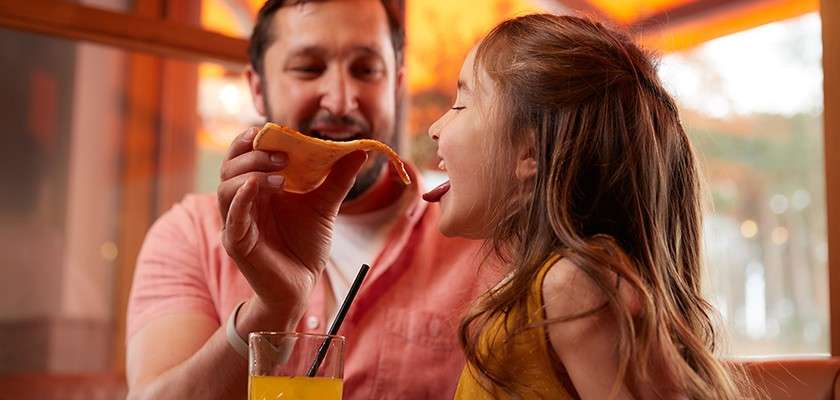 A father feeding his daughter a slice of pizza