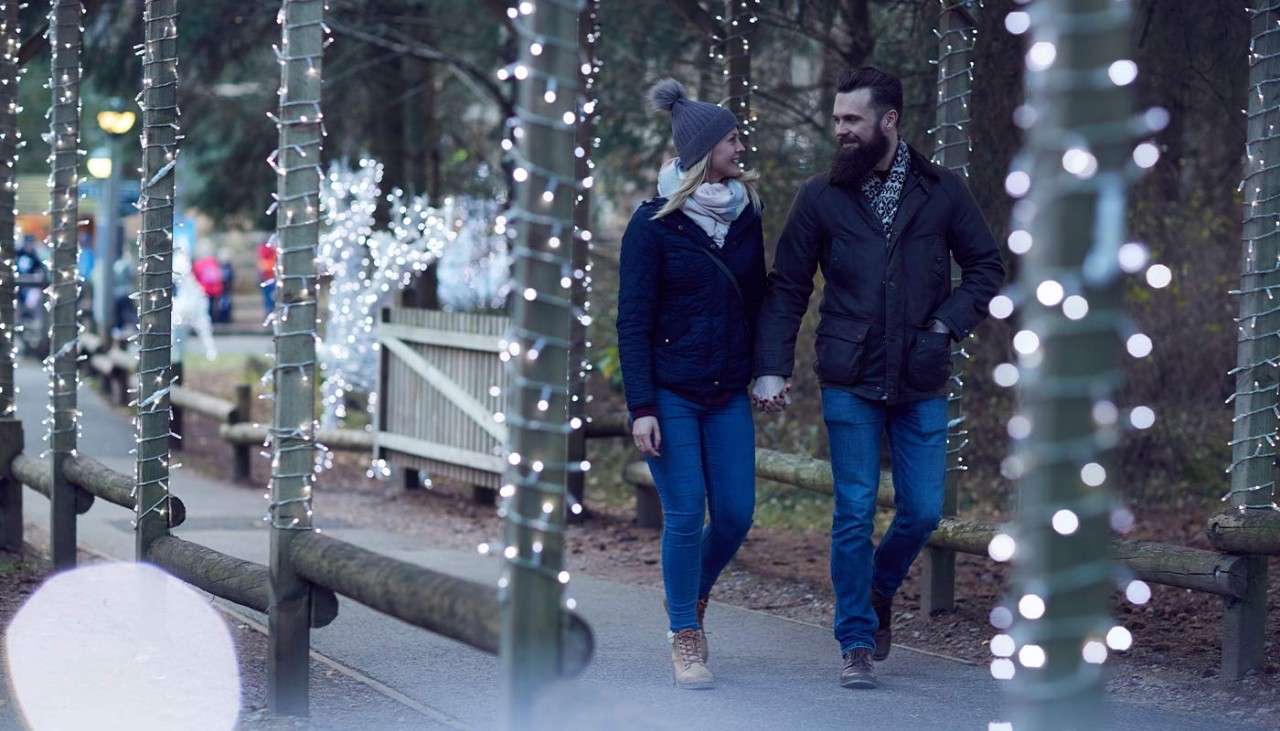 Couple holding hands as they walk through Winter Wonderland where the pathway is decorated with Christmas lights