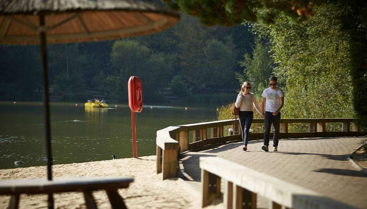 Couple walking along a path beside a Center Parcs lake and the beach