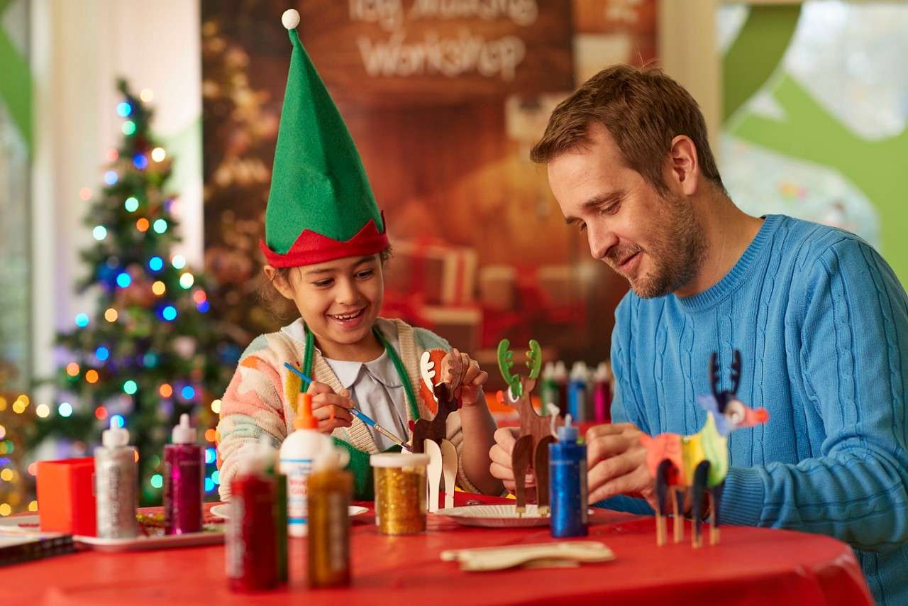 Girl with an elf hat making toys with an adult.