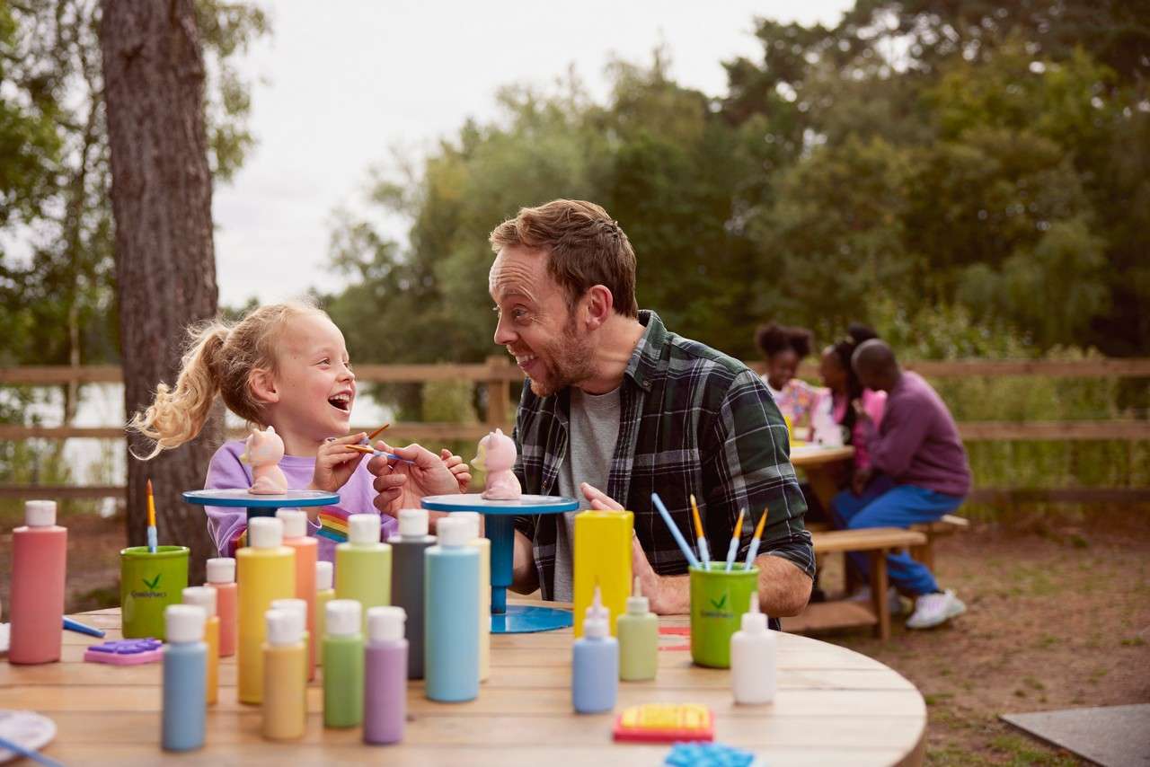 Girl painting pottery with an adult outside.