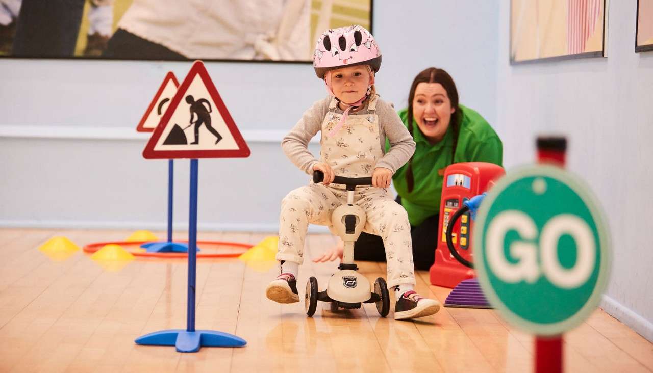 Young girl riding a scooter around an indoor course