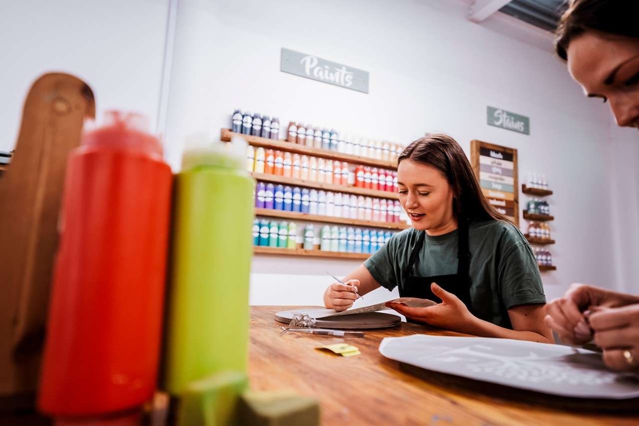 Woman painting a wooden plank inside the Woodcraft Workshop.