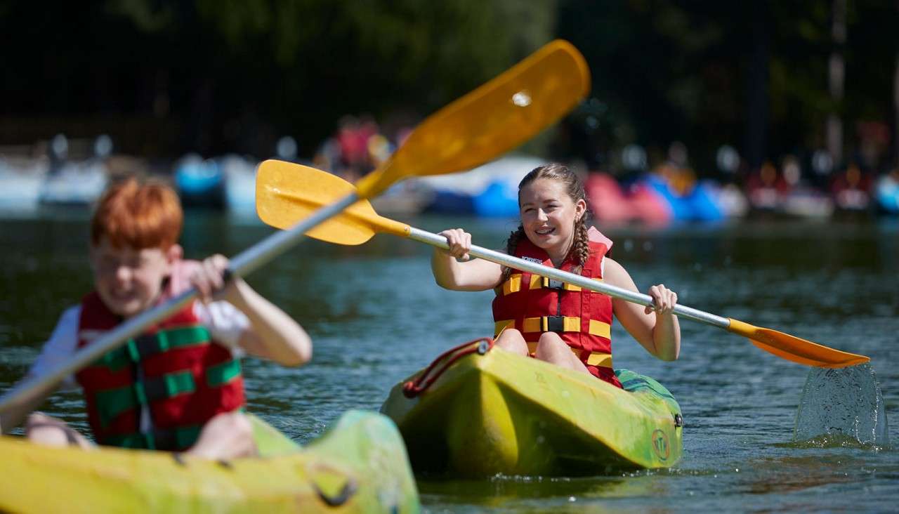 Two young people paddling kayaks on the lake.