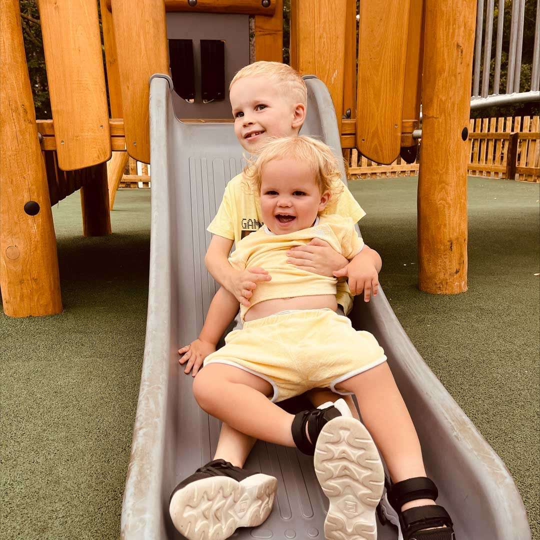 Two young boys sliding down a slide whilst holding onto one another