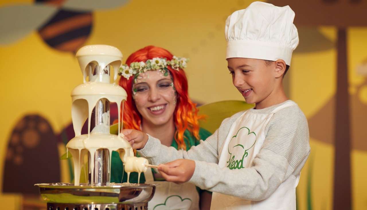 Young boy dressed as a chef, collecting chocolate from a flowing chocolate fountain.