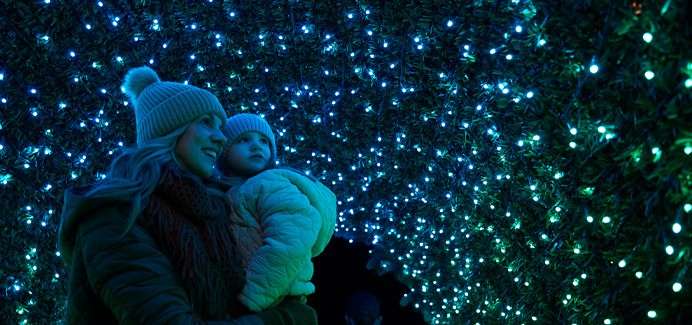 Woman holding a young girl as they admire sparkling Christmas lights.
