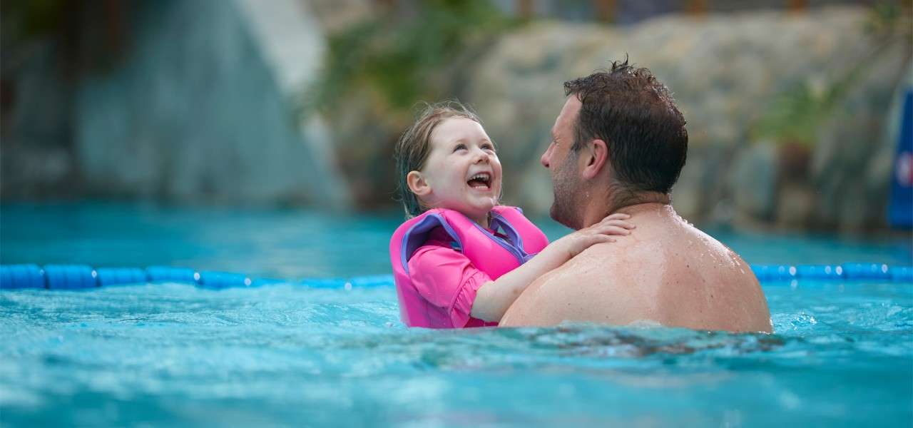 Young girl being held by her father in a pool.