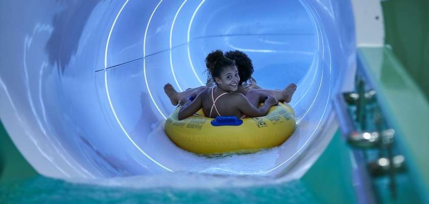 Two children on a pool inflatable about to start riding down a waterslide.