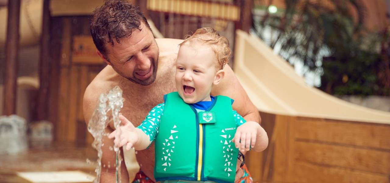 A father and his toddler playing in a water play area of the Subtropical Swimming Paradise