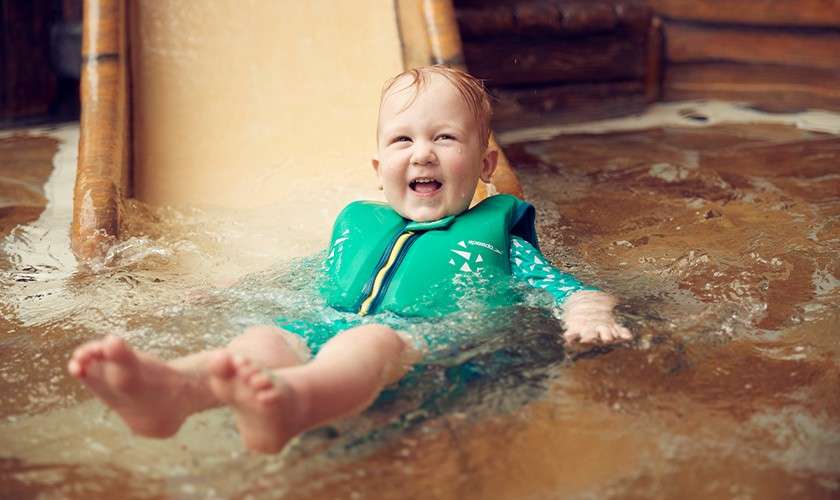 A pre school aged child laughing as he reaches the bottom of the slide. 