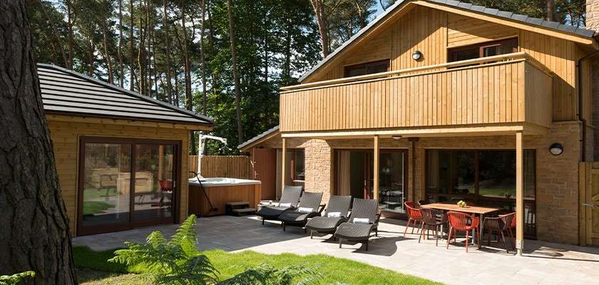 A hot tub with a hoist and a sauna building on the patio outside an adapted Exclusive Lodge 