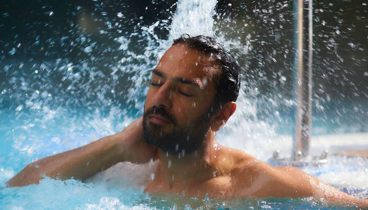 Man soaking under a water jet in the outdoor pool.