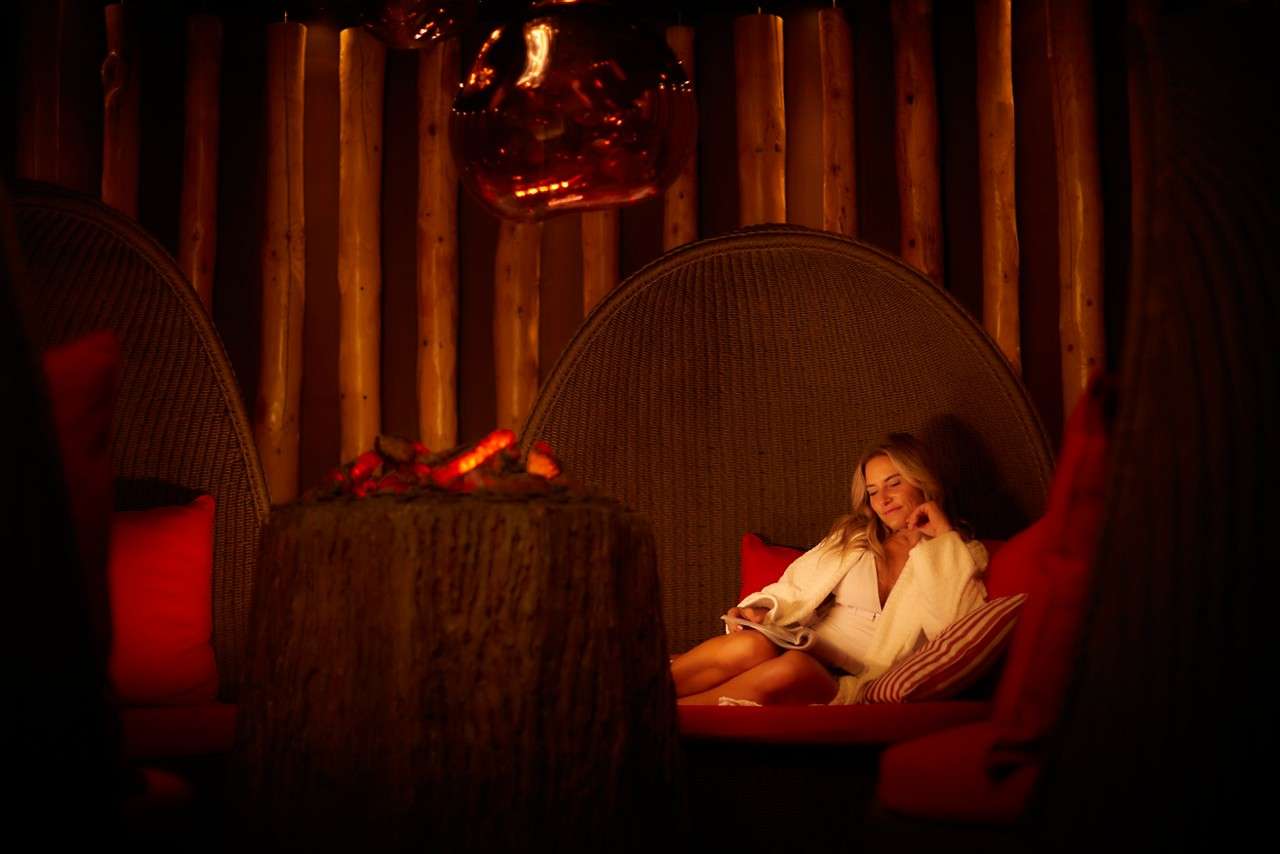 Woman reading as she lounges in a cosy cocoon chair inside the Fireside Relax.