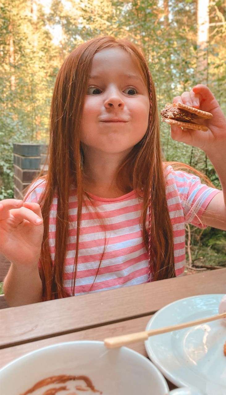 A girl eating on a bench outside her lodge whilst surrounded by the forest.