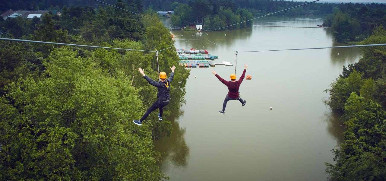 Two people ziplining across a lake 