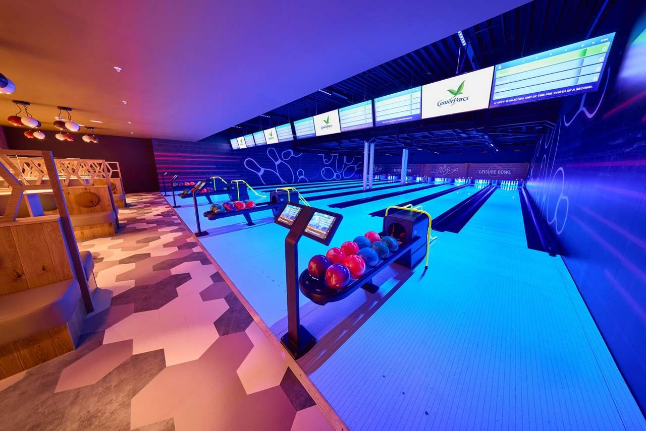 Bowling lanes sit ready, balls racked and scoring kiosks lit, in a neon-blue alley with left-side booth seating. Text: CenterParcs; LEISURE BOWL.