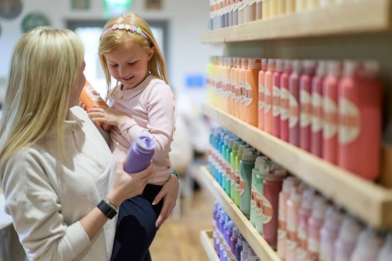 A little girl being held by an adult while she picks out paint colours.