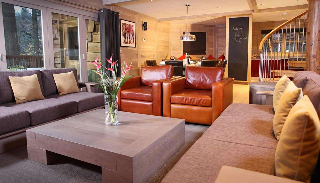 A treehouse living area. In the foreground are two sofas, two armchairs and a coffee table with a vase of flowers.