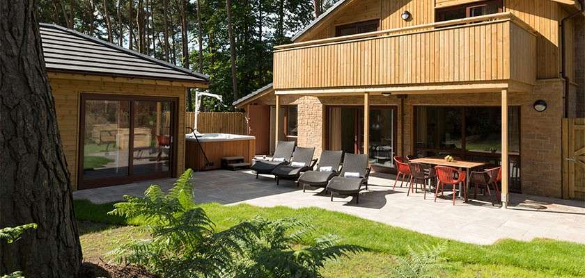 The exterior of an adapted lodge showing sun loungers and a hot tub with hoist.