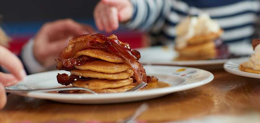 A stack of pancakes with bacon and syrup.
