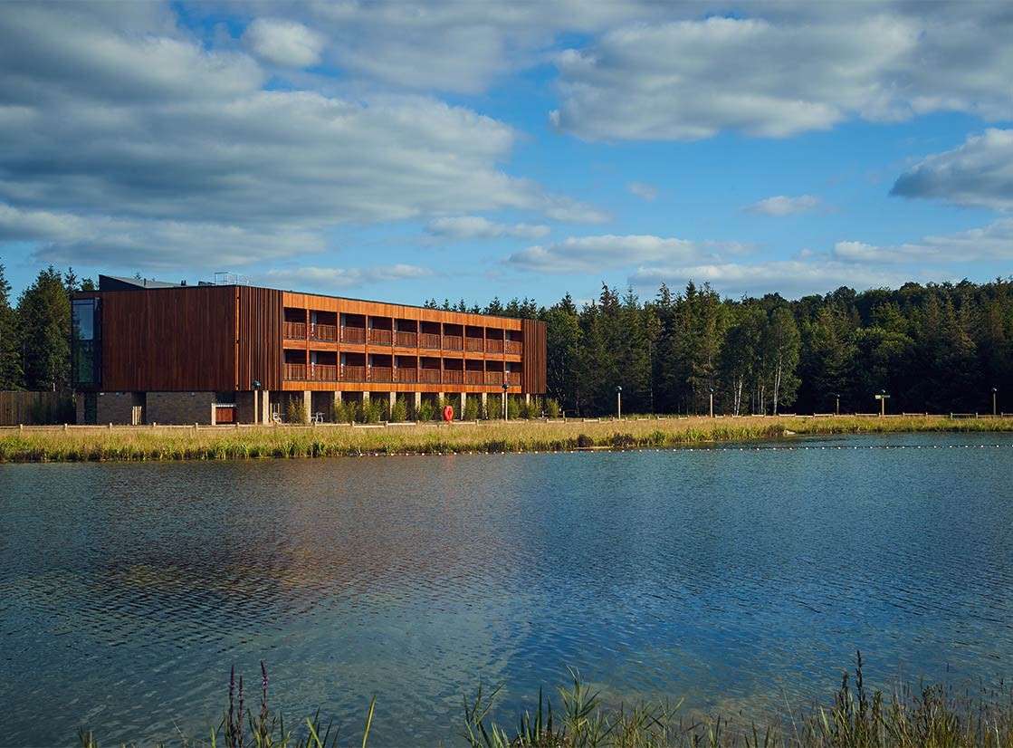 An apartment with a neatly made double bed and a balcony facing into the forest available at Longleat Forest 