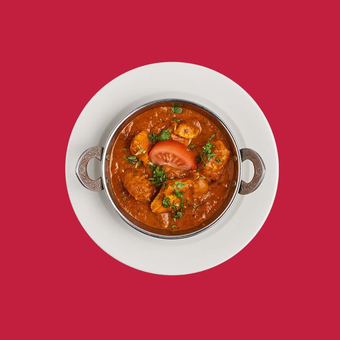Chicken bhuna served with a slice of tomato in a traditional bowl.