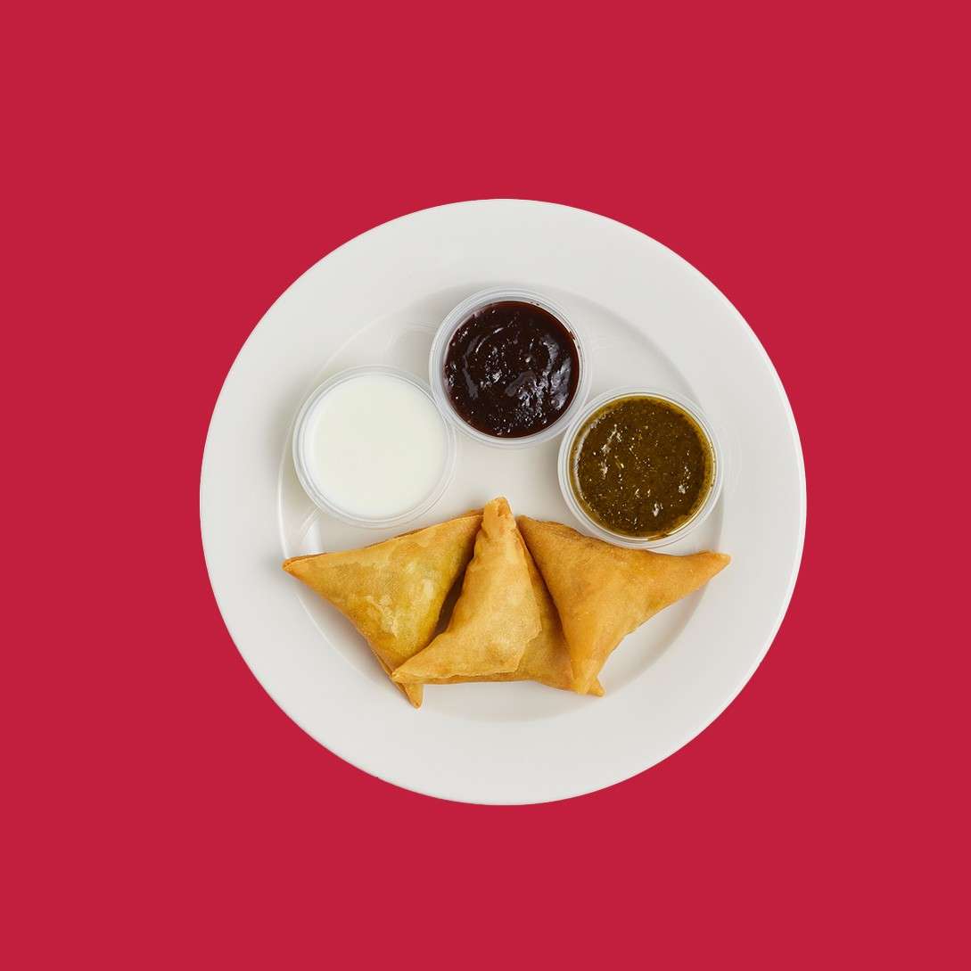 Three triangular samosas with a trio of dipping sauces.