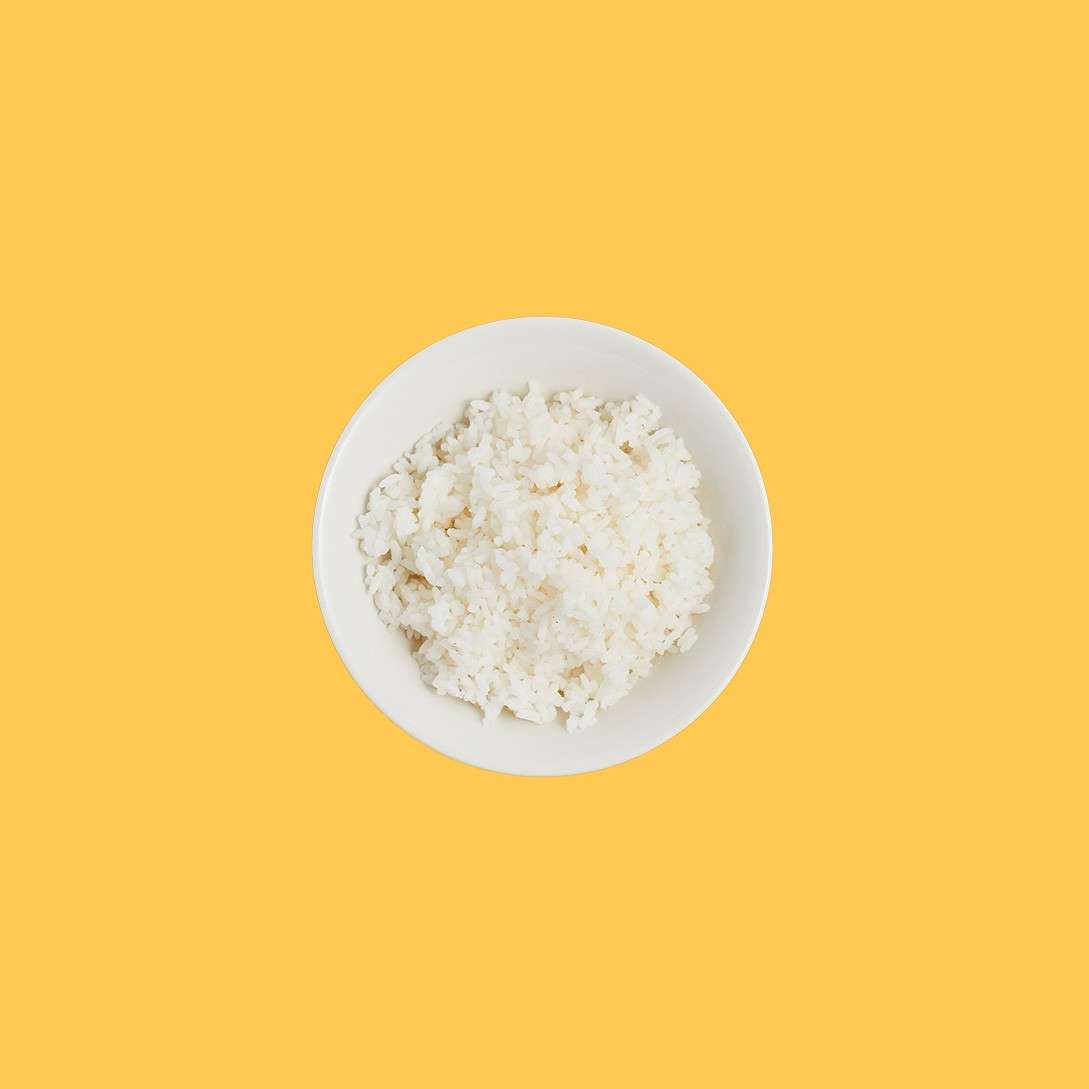 White bowl of steamed rice sits centered against a solid yellow background.