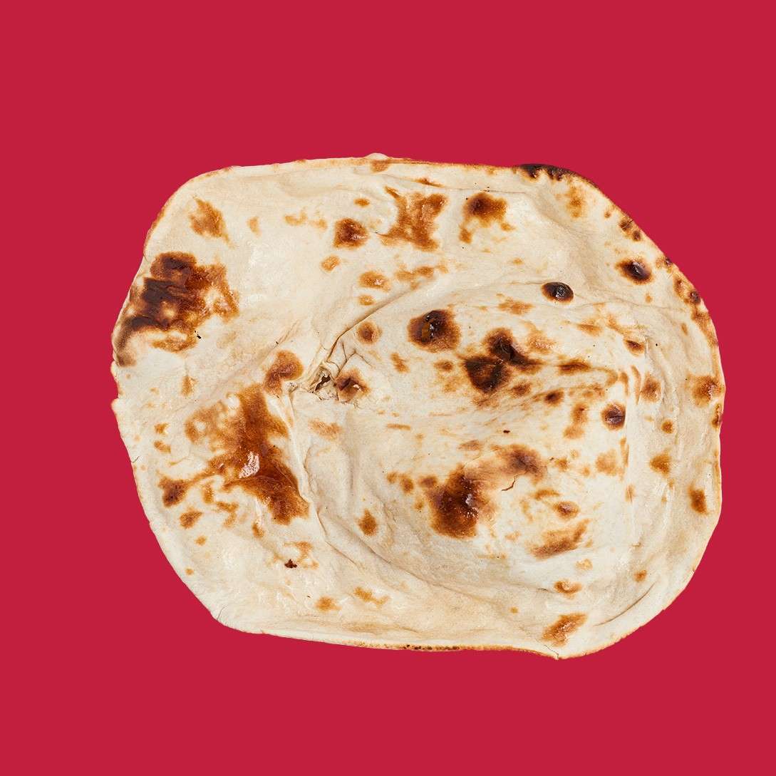 An irregular oval flatbread sits slightly puffed, showing brown char blisters and soft pale dough, centered against a plain red background.